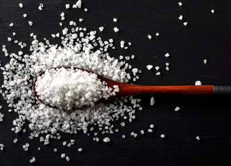 Sea Salt in Bamboo Wooden Spoon on black stone background