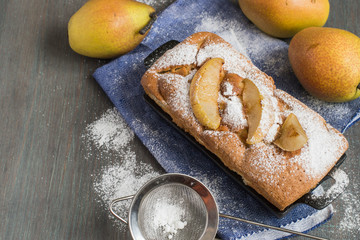 Sweet dessert. Freshly baked homemade pie with fruit filling, fresh pears and a strainer with powdered sugar on an old wooden table.