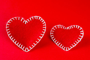 two decorative  hearts made of red fumirana sewn with a white thread, on a red background. Happy Valentine's Day symbol. selective focus. close-up. can be used as a background