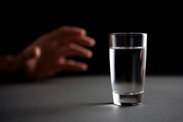 hand reaches for a glass of vodka or alcohol drink, alcoholism and alcohol abuse concept, defocused,.selective focus, close up, gray table, dark background