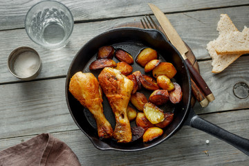 Fried chicken legs, fried potatoes in frying pan, top view