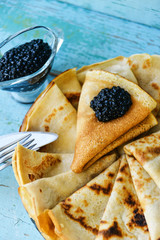 Pancakes with black caviar and sour cream on a wood table in a white plate
