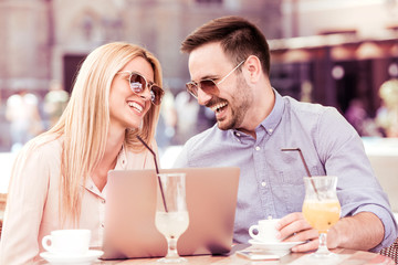 Happy young man and woman using laptop in the city.