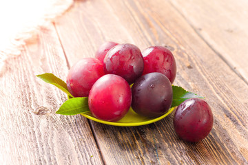 Ripe plums lie in a saucer on a wooden table