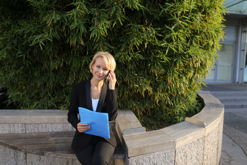 Businesswoman talking with partner by smartphone outdoors and keeping blue document case. Concept...
