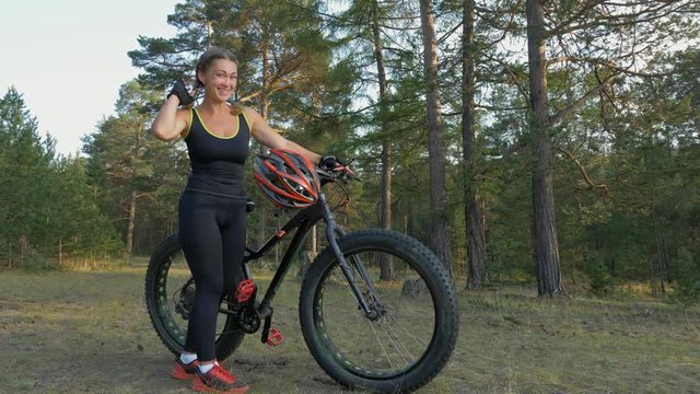 Fat bike also called fatbike or fat-tire bike in summer riding in the forest. Beautiful girl and her bicycle in the forest. She is posing and pampering near the bicycle.