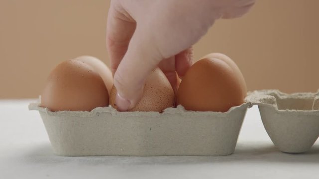 woman's hand puts egg box to the table, open it and take one of it. closeup front view