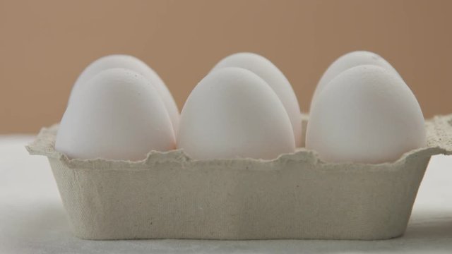 closeup of woman's hand put the egg box with white eggs on thetable and open it. front view