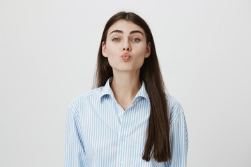 Obraz premium Indoor shot of attractive brunette folding lips and bending towards camera as if waiting for kiss, expressing desire and awaitness. Girlfriend recieves her kiss from boyfriend who came home from work