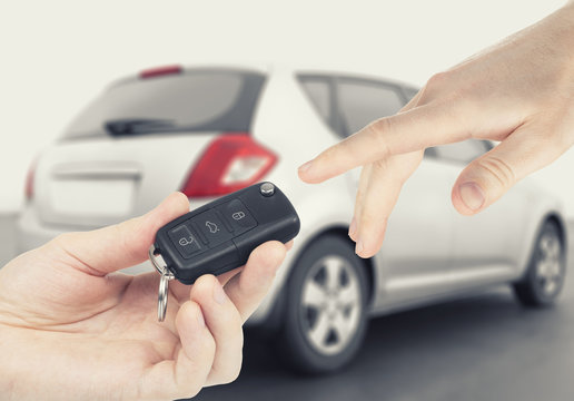 One person passing car-keys to another person with car on background