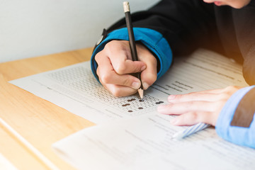 Naklejka premium high school or university student hands taking exams, writing examination on paper answer sheet optical form of standardized test on desk doing final exam in classroom. Education literacy concept.
