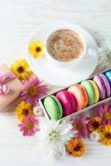 Photo of cake macarons, gift box, tea, coffee, cappuccino and flowers. Sweet romantic food macaroon concept. Morning breakfast and presents.