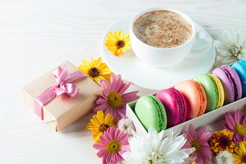 Photo of cake macarons, gift box, tea, coffee, cappuccino and flowers. Sweet romantic food macaroon concept. Morning breakfast and presents.