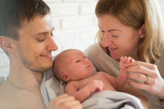 Portrait of young happy man and woman holding newborn cute babe . Caucasian smiling father and mother embracing tenderly adorable new born child. Happy family concept. Deadpan raw photo nofilter