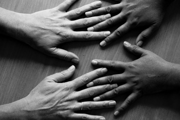 looking down on four hands, fingers spread out, lying flat on a table, the two hands on the left are Asian hands and the two hands on the right are caucasian hands