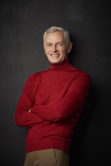 Casual senior man portrait. Handsome elderly man wearing red turtle neck sweater and looking at camera while standing against at dark background.