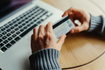 Cropped shot of a man's hands using a laptop at home while holding credit card in the hands, on-line shopping at home, cross process, filtered image