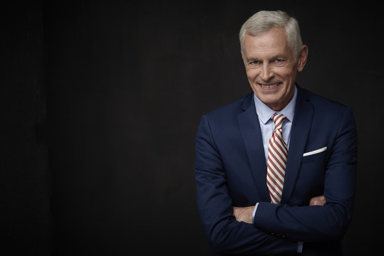 Smiling business man portrait. Executive senior lawyer businessman wearing suit and looking at camera while standing at isolated black background with copy space. 