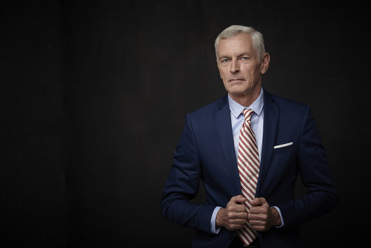 Confident businessman portrait. Executive senior lawyer businessman wearing suit and looking at camera while standing at isolated black background with copy space. 