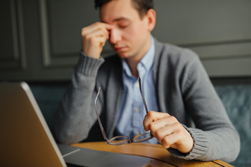 Feeling sick and tired. Frustrated young man massaging his nose and keeping eyes closed while sitting while working in cafe.