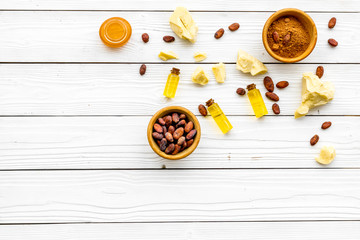 Pieces of cocoa butter and cacao powder in bowl for homemade cosmetics. White wooden background top view space for text