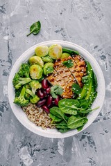 Healthy buddha bowl lunch with grilled chicken, quinoa, spinach, avocado, brussels sprouts, broccoli, red beans with sesame seeds
