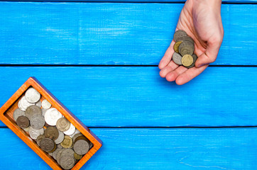 money in hand, casket with coins on a blue wooden background, space for text