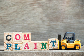 Toy forklift hold letter block T to complete word complaint on wood background