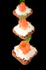 Canape with salmon and cream cheese on black background