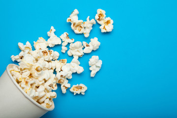 Spilled popcorn from a paper bucket or a cup on a blue background.
