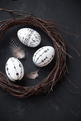 Easter concept with a rustic handmade wreath and three decorated eggs against blask wooden background © kuvona