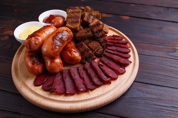 Appetizing beer snacks close up. Grilled sausages with dried meat basturma, crunchy toasts and sauces, Oktoberfest food, pub concept