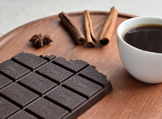 Coffee mood. Close up of a cup of coffee, a chocolate bar, three cinnamon sticks on a wooden background