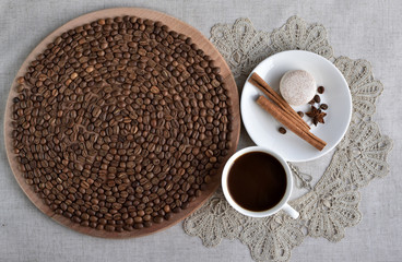 Coffee mood. A cup of coffee, coffee beans on a round wooden board, macaroon, cinnamon steaks, anise star and rustic lace.