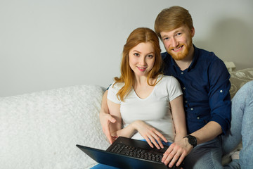 beautiful young couple guy with a girl with red hair sitting on the couch with a laptop