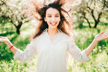 Expressive portrait of young cheerful emotional model girl throwing hair. Spring is coming. Cute funny unusual female person enjoying innocence of life outdoor in blooming garden with blossom flowers.