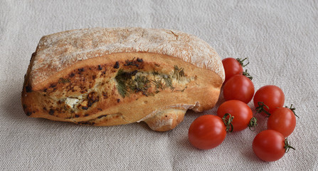 Ciabatta bread and cherry tomatoes. Rustic bread with soft cheese and herbs lies on linen cloth.