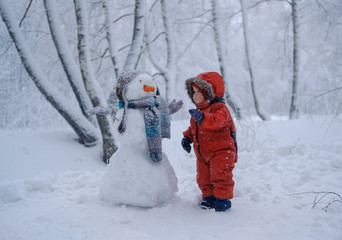 Fototapeta na wymiar European boy and the snowman in a snowy forest