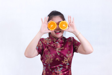 Portrait of Beautiful Young asian woman wear chinese dress traditional cheongsam or qipao. holding orange slices in front of her eyes and smile. healthy eating diet concepts. healthy food concept.