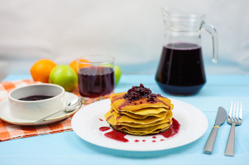 Pancakes with raspberry jam and grape juice on a blue background