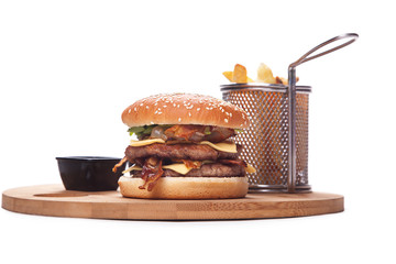 double burger with cheddar and bacon,Burger with french fries on a round wooden board,ketchup and mayonnaise in black pots.isolated on white background