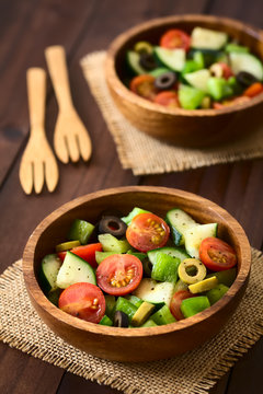 Fresh salad of black and green olives, cherry tomato, green bell pepper, cucumber, salt, pepper, dried oregano and basil, photographed with natural light (Selective Focus in the middle of first salad)