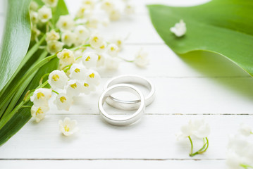 Lily of the valley with wedding rings on white wooden