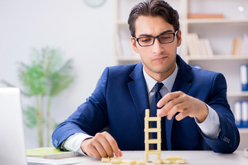 Young businessman building domino tower in office