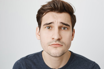 Fototapeta premium Close-up portrait of cute attractive european man showing puppy look with lifted eyebrows and innocent smile, standing over gray background. Guy stands near door and begs for forgiveness.