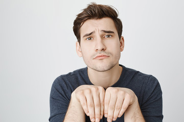 Cute caucasian man imitating puppy showing paws with hands, frowning eyebrows, standing over gray...