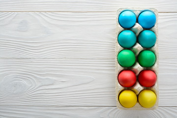 Colorful easter eggs in a tray on a white wooden background. Top view