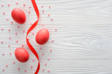 Arrangement of red Easter eggs with ribbon on wooden background. Top view with copy space
