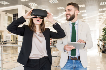 Portrait of modern young woman trying on VR helmet in mall and looking excited