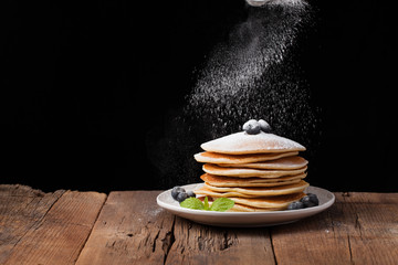 Pancakes with blueberries and honey on a wooden rustic table. Dessert for Breakfast on a black background. Copy space for your text